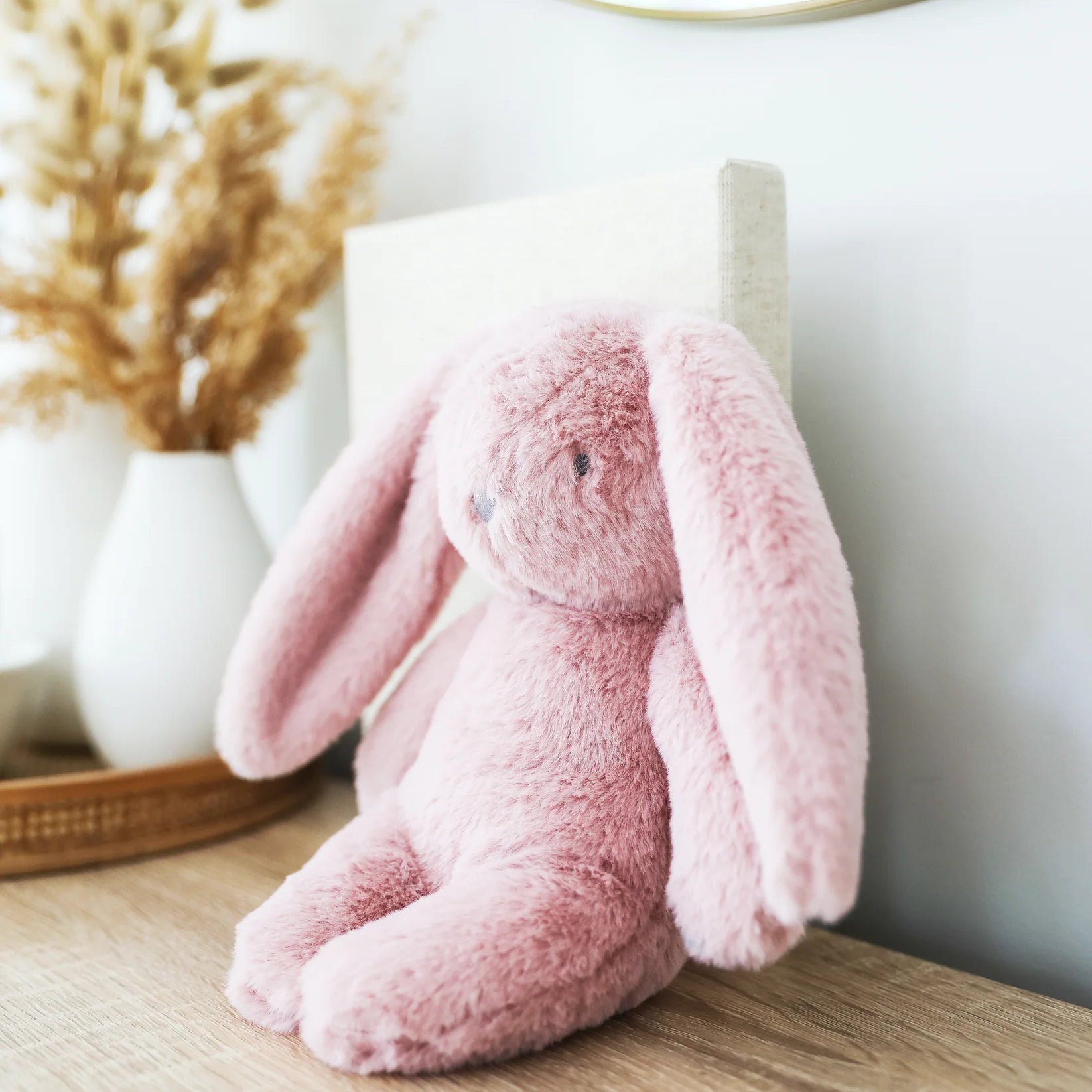 Alimrose Darcey Plush Baby Bunny 27cm in petal pink sitting on a wooden dresser in a nursery setting.