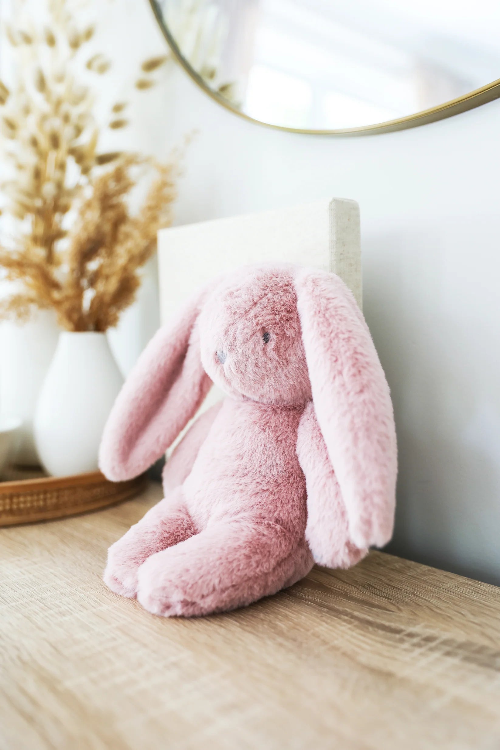 Alimrose Darcey Plush Baby Bunny 27cm in petal pink sitting on a wooden dresser in a nursery setting.