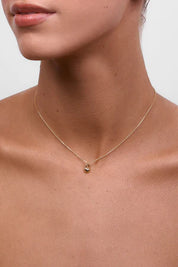 A model wearing the delicate gold chain necklace with a small heart-shaped lock pendant, sitting just above the collarbone.