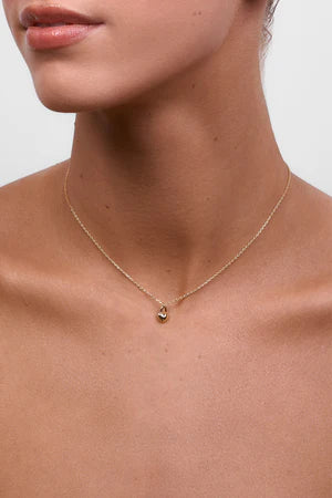 A model wearing the delicate gold chain necklace with a small heart-shaped lock pendant, sitting just above the collarbone.