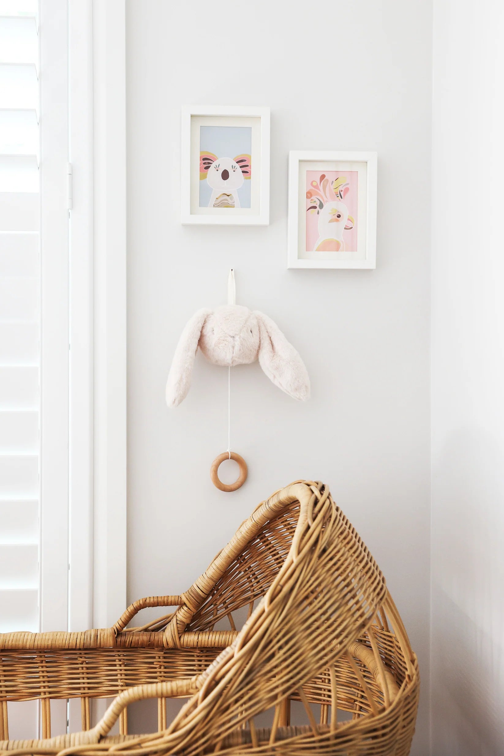 Alimrose Darcey Bunny Musical toy in ivory, hanging on nursery wall above wicker bassinet with framed artwork.