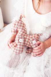 Child in white dress holding Alimrose Jointed Pony 22cm in rose check fabric with button joints.
