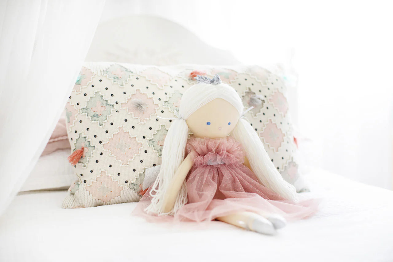 Alimrose Penelope Princess doll 50cm wearing sparkle blush tulle dress and silver crown, sitting on a bed with decorative pillow.