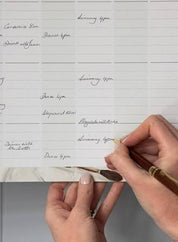 Hands writing in Bespoke Letterpress 2026 Family Wall Calendar with six organizational columns and Australian public holidays.