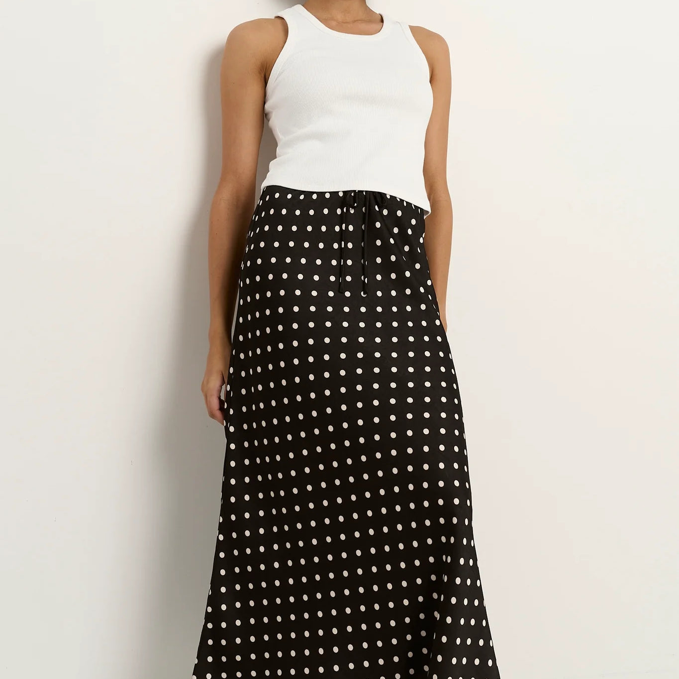 Black white polka dot satin maxi skirt styled with white tank top casual chic outfit bias cut silhouette comfortable elastic waist timeless wardrobe essential