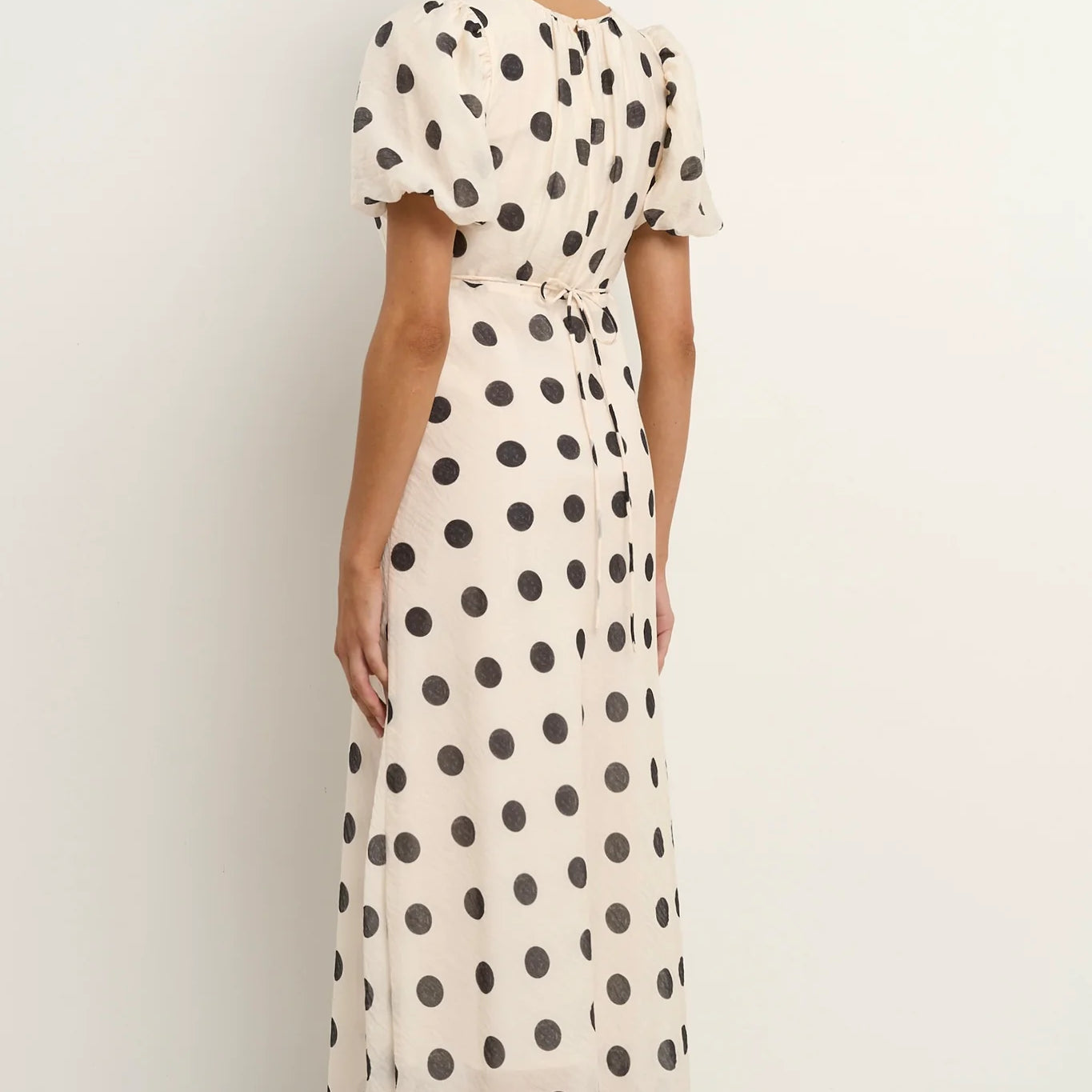 Cream black polka dot maxi dress side sitting view feminine puff sleeve design gathered neckline fitted waist flowing skirt bias cut silhouette soft breathable tencel nylon blend fabric