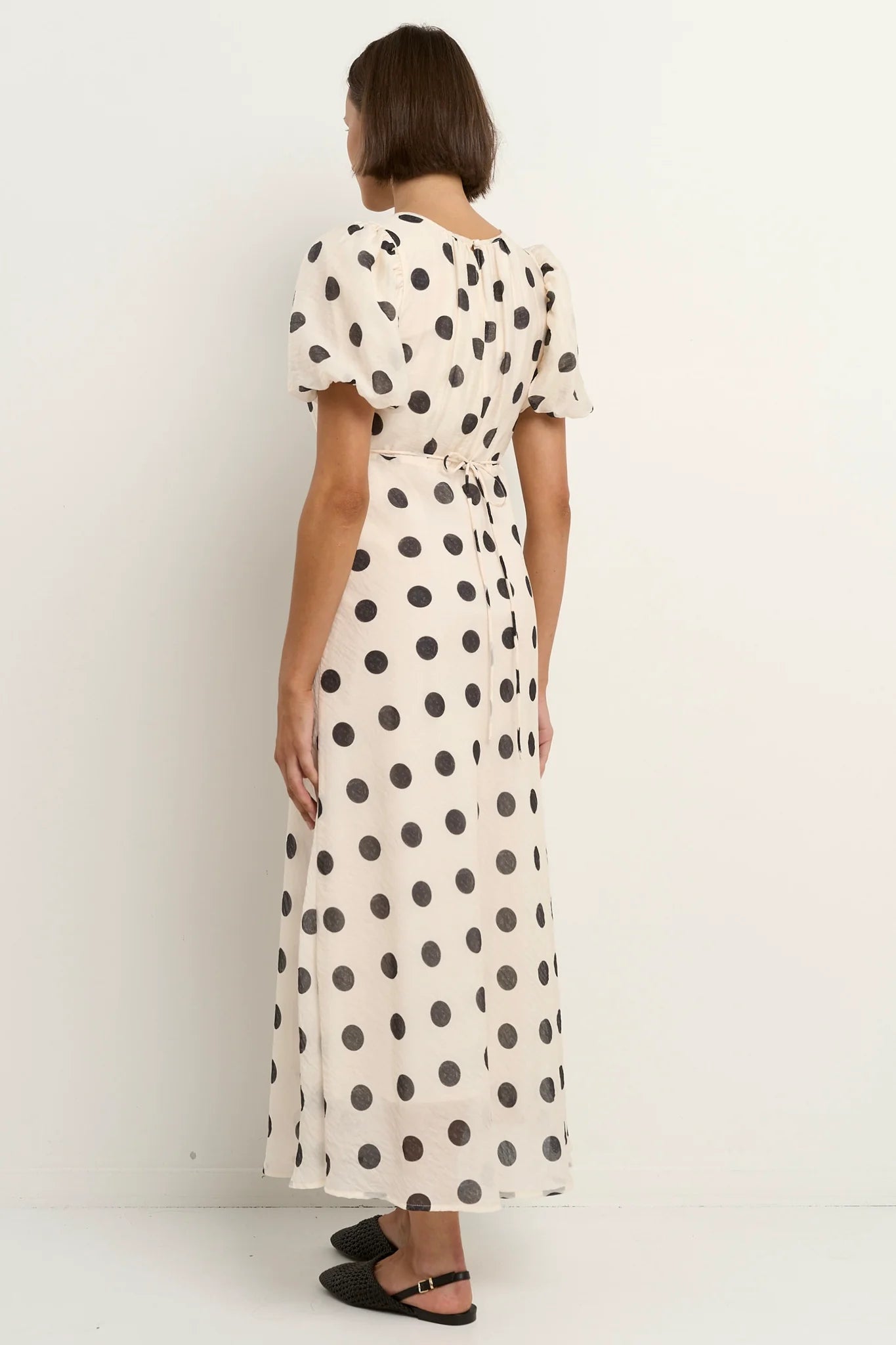 Cream black polka dot maxi dress side sitting view feminine puff sleeve design gathered neckline fitted waist flowing skirt bias cut silhouette soft breathable tencel nylon blend fabric