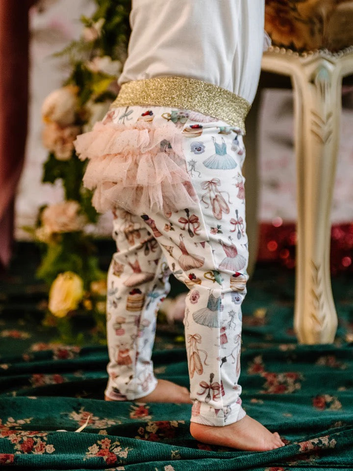 Close up of toddler in patterned leggings with gold waistband and layered pink tulle frill on back
