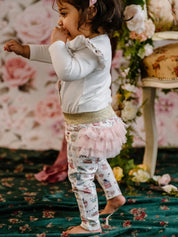 Toddler standing in frilled leggings featuring pastel party motifs with pink tutu detail and gold waistband