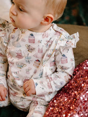 Close up of frill coverall fabric with detailed party themed illustrations including cakes ballet outfits and teacups