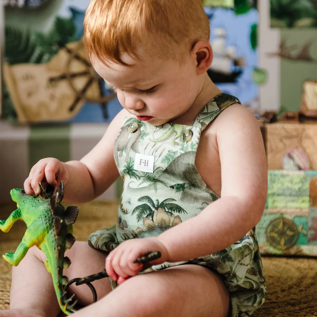Toddler playing with dinosaur toy while wearing Fleur Harris Prehistorica Brontis Romper in Olive Leaf print.