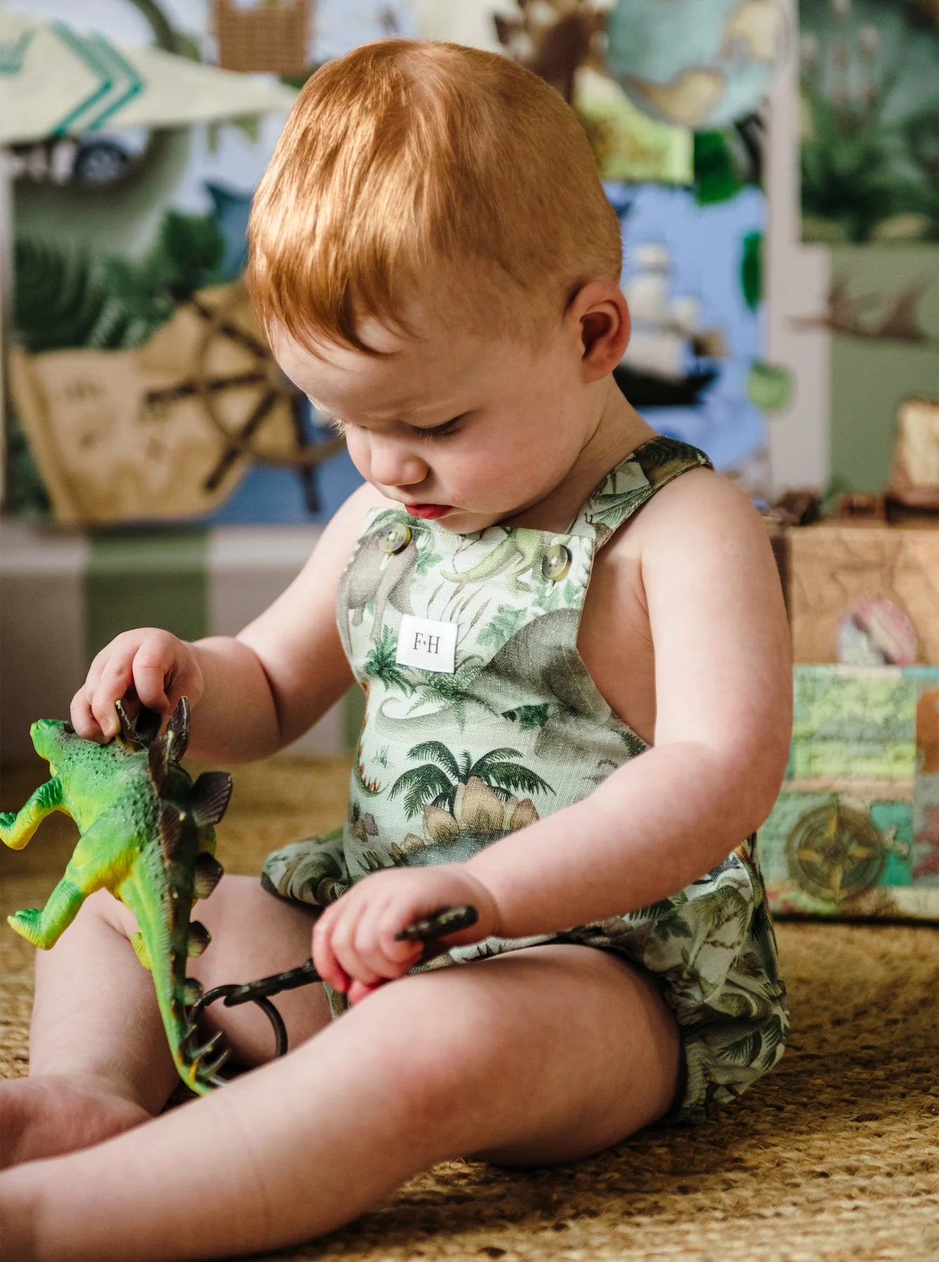Toddler playing with dinosaur toy while wearing Fleur Harris Prehistorica Brontis Romper in Olive Leaf print.