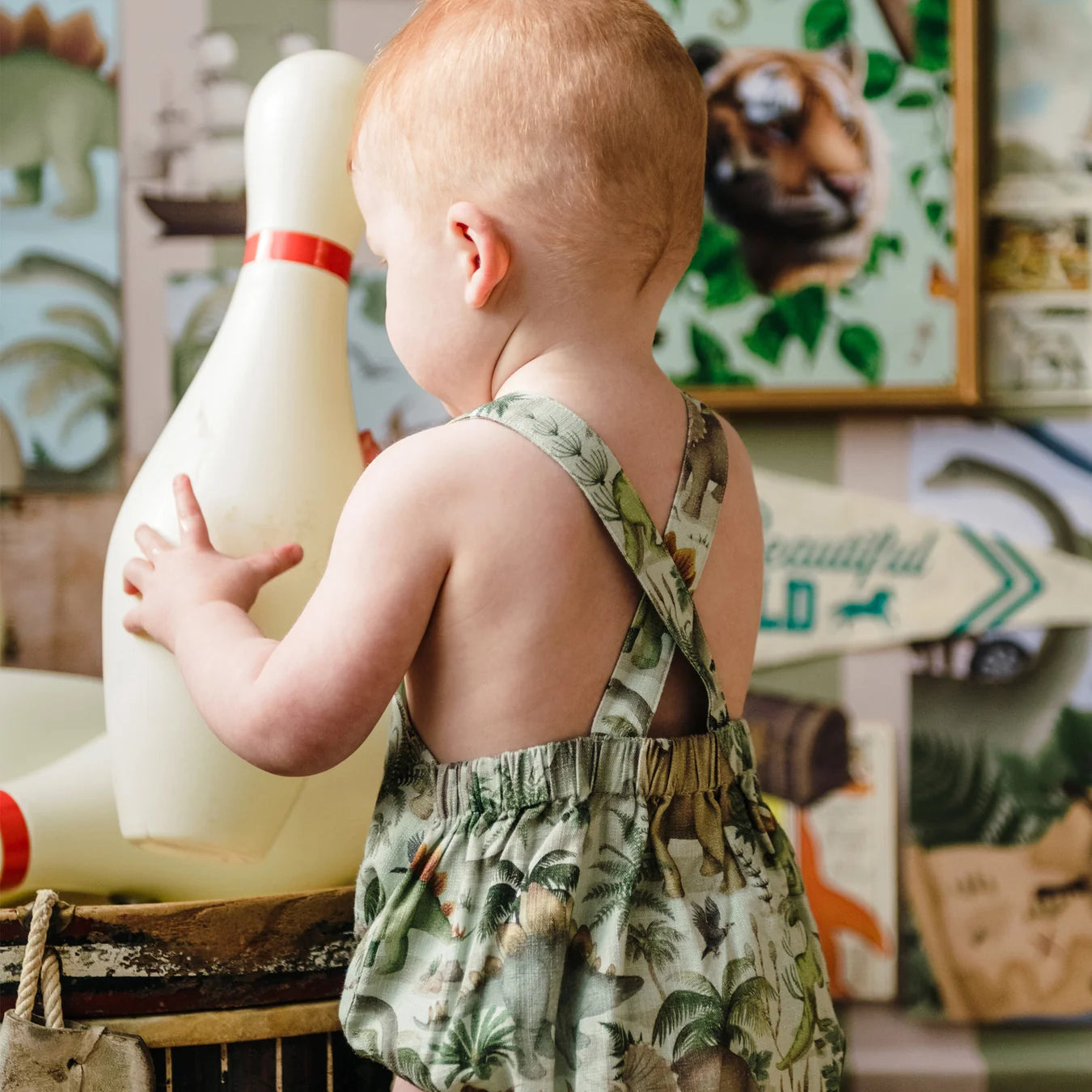Baby wearing Fleur Harris Prehistorica Brontis Romper in Olive Leaf dinosaur print, side view.