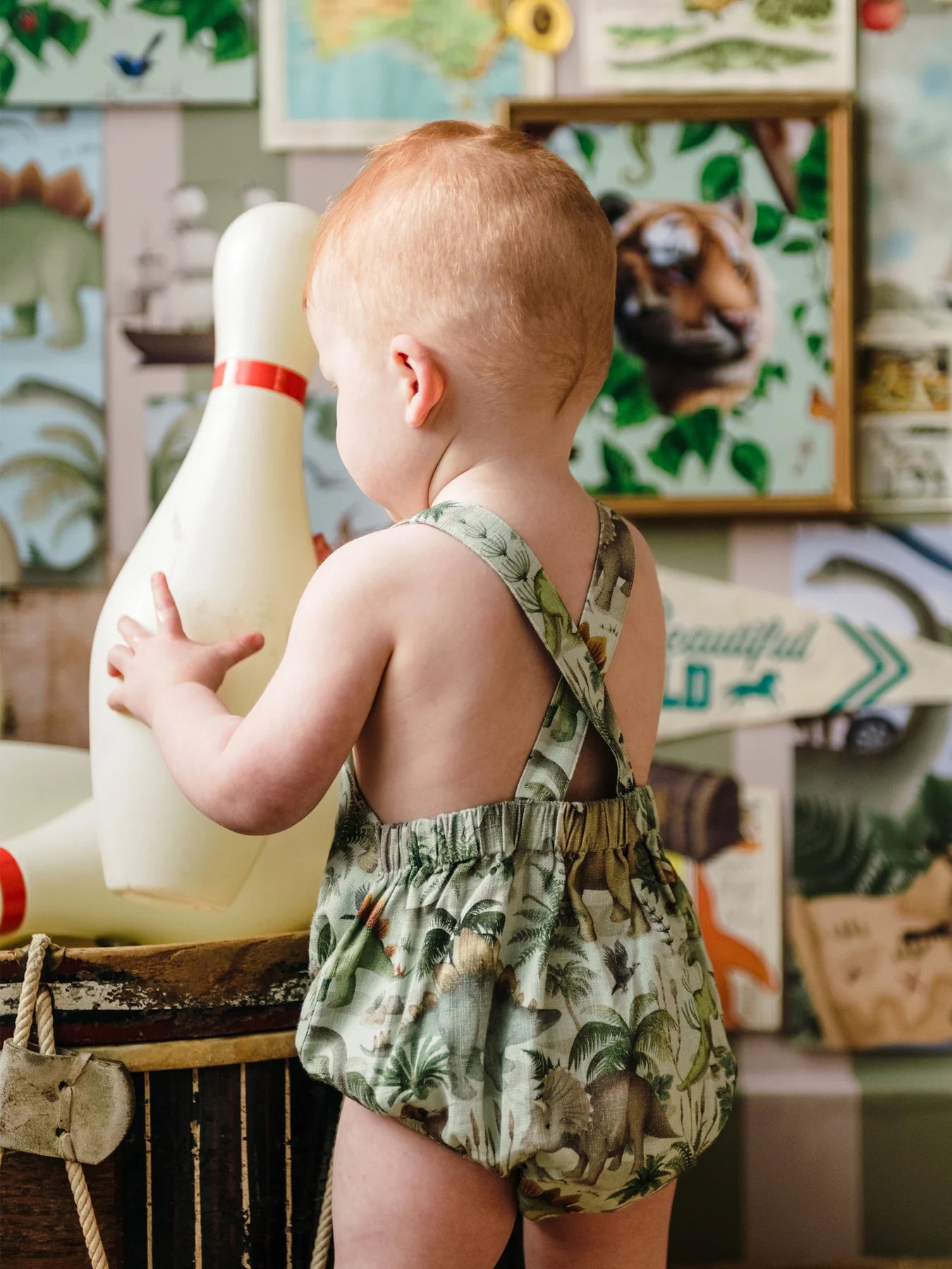 Baby wearing Fleur Harris Prehistorica Brontis Romper in Olive Leaf dinosaur print, side view.