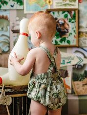 Baby wearing Fleur Harris Prehistorica Brontis Romper in Olive Leaf dinosaur print, side view.