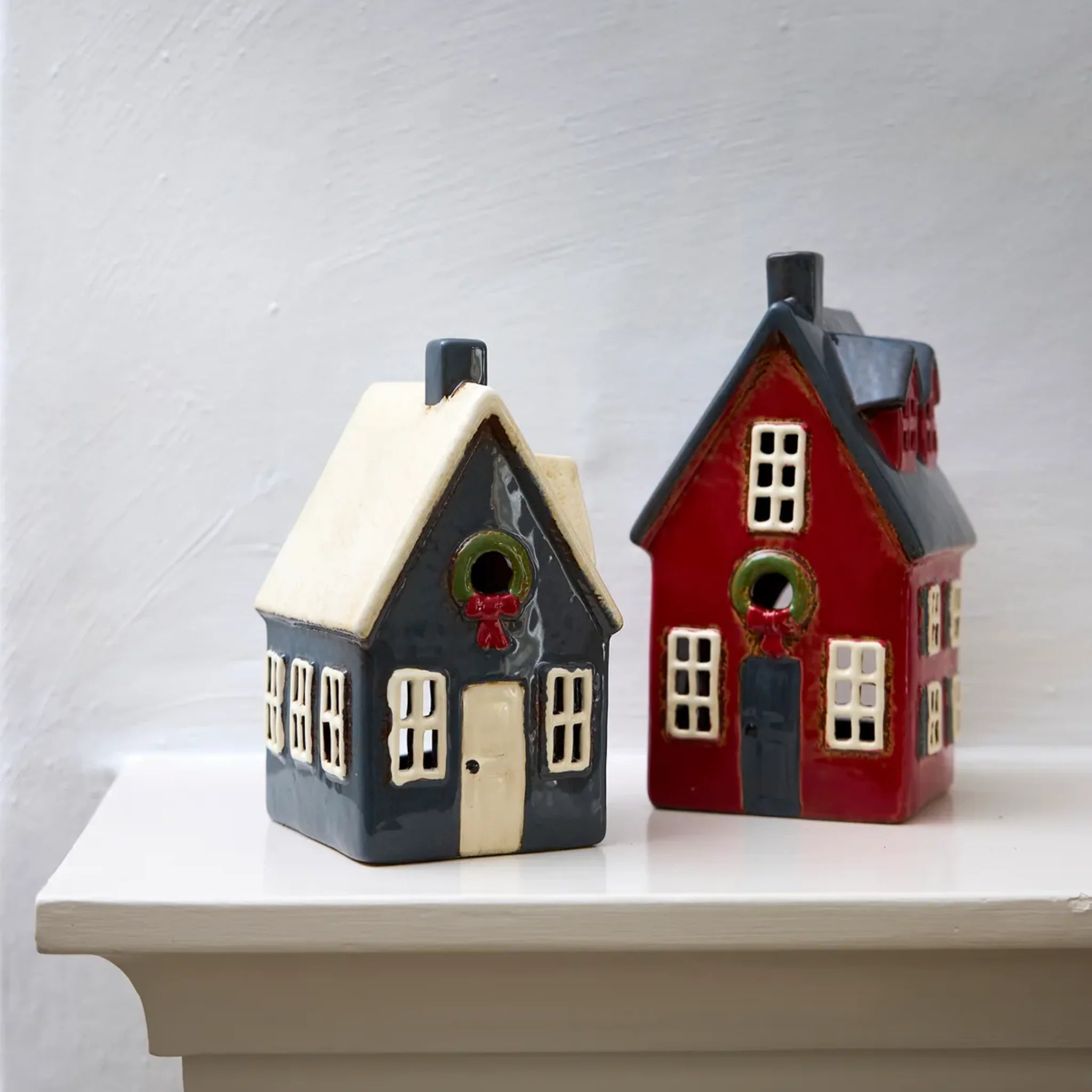 Display of French Country Alsace Tea Light Cottage in red with wreath beside a grey cottage on a mantel.