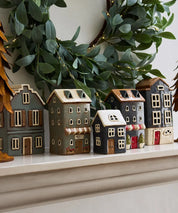Collection of ceramic tea light houses styled on a mantel with greenery, featuring navy house with white roof in the center