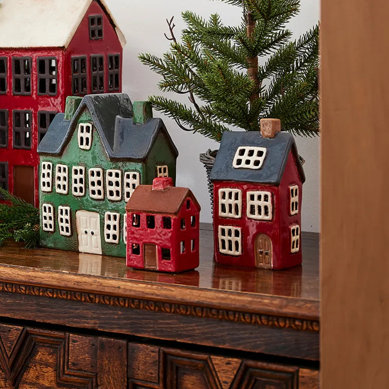 French Country ceramic Christmas tea light houses including Alsace House with navy roof, displayed with festive greenery.