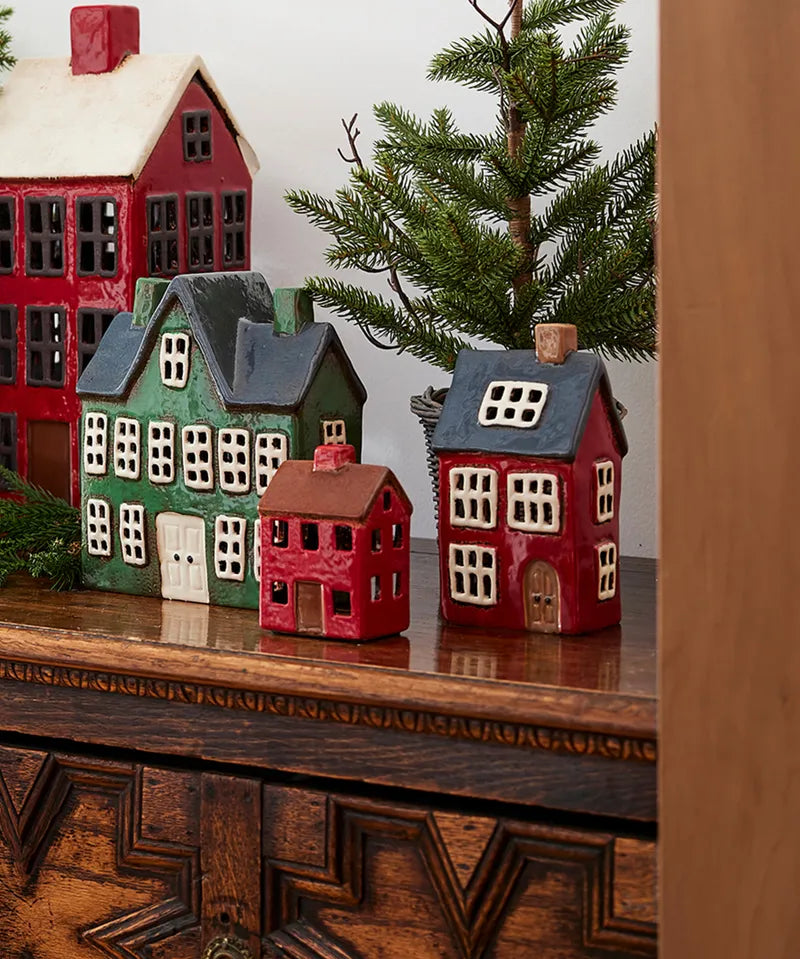 French Country ceramic Christmas tea light houses including Alsace House with navy roof, displayed with festive greenery.