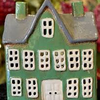 Front view of green ceramic tea light manor house with grey gabled roof, white door, and multiple square cut-out windows