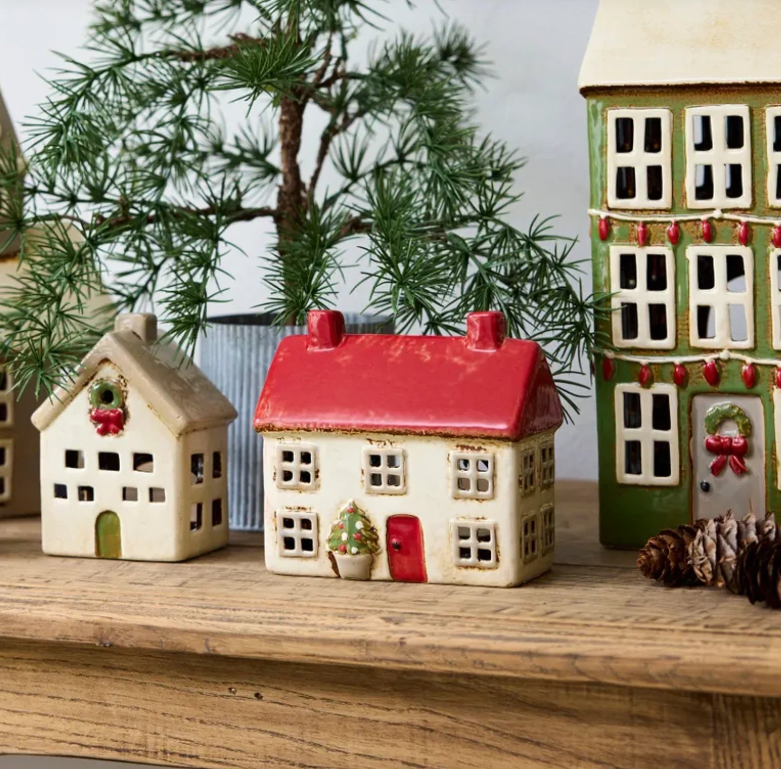 Christmas display of ceramic tea light houses on wooden surface, featuring stone villa with wreath, red-roof villa, and green townhouse