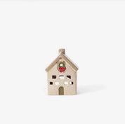 Small stone-colored ceramic tea light villa with square windows and green door, decorated with a red Christmas wreath