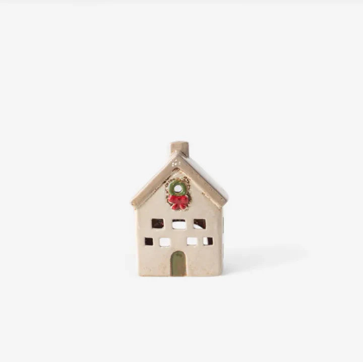 Small stone-colored ceramic tea light villa with square windows and green door, decorated with a red Christmas wreath
