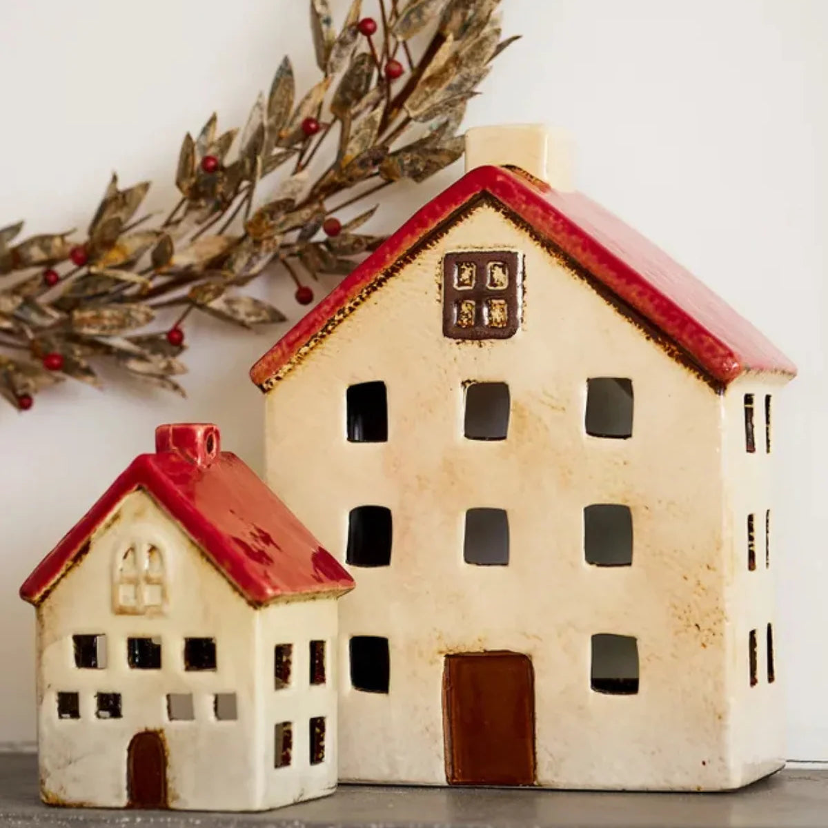 Two ceramic tea light houses in white with red roofs styled on a mantel with festive wreath