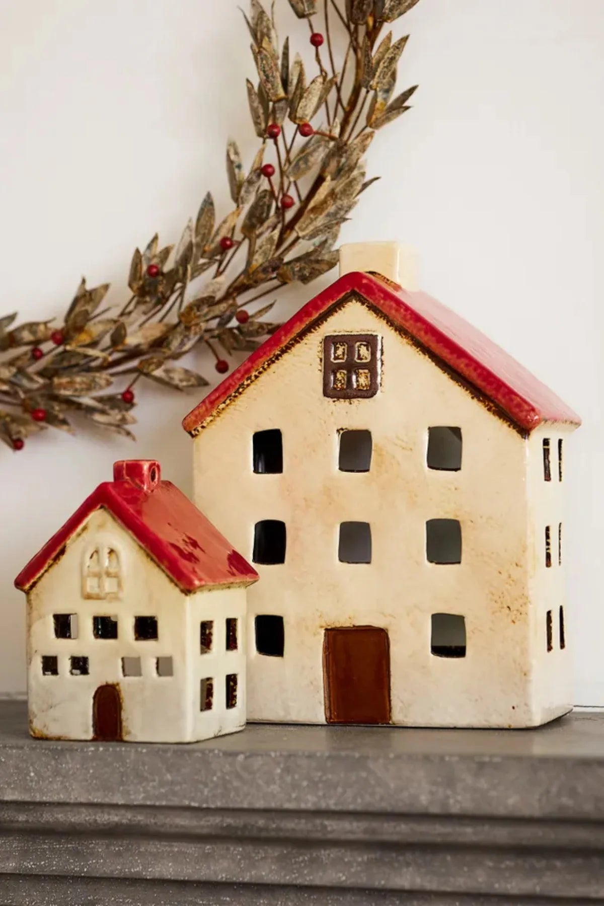 Two ceramic tea light houses in white with red roofs styled on a mantel with festive wreath