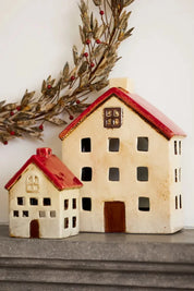 Two ceramic tea light houses in white with red roofs styled on a mantel with festive wreath