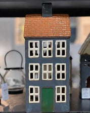 Decorative ceramic tea light chalet with navy walls, green door, and terracotta roof displayed indoors.
