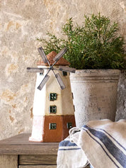 Decorative ceramic windmill tea light house displayed on a wooden table with rustic planter background