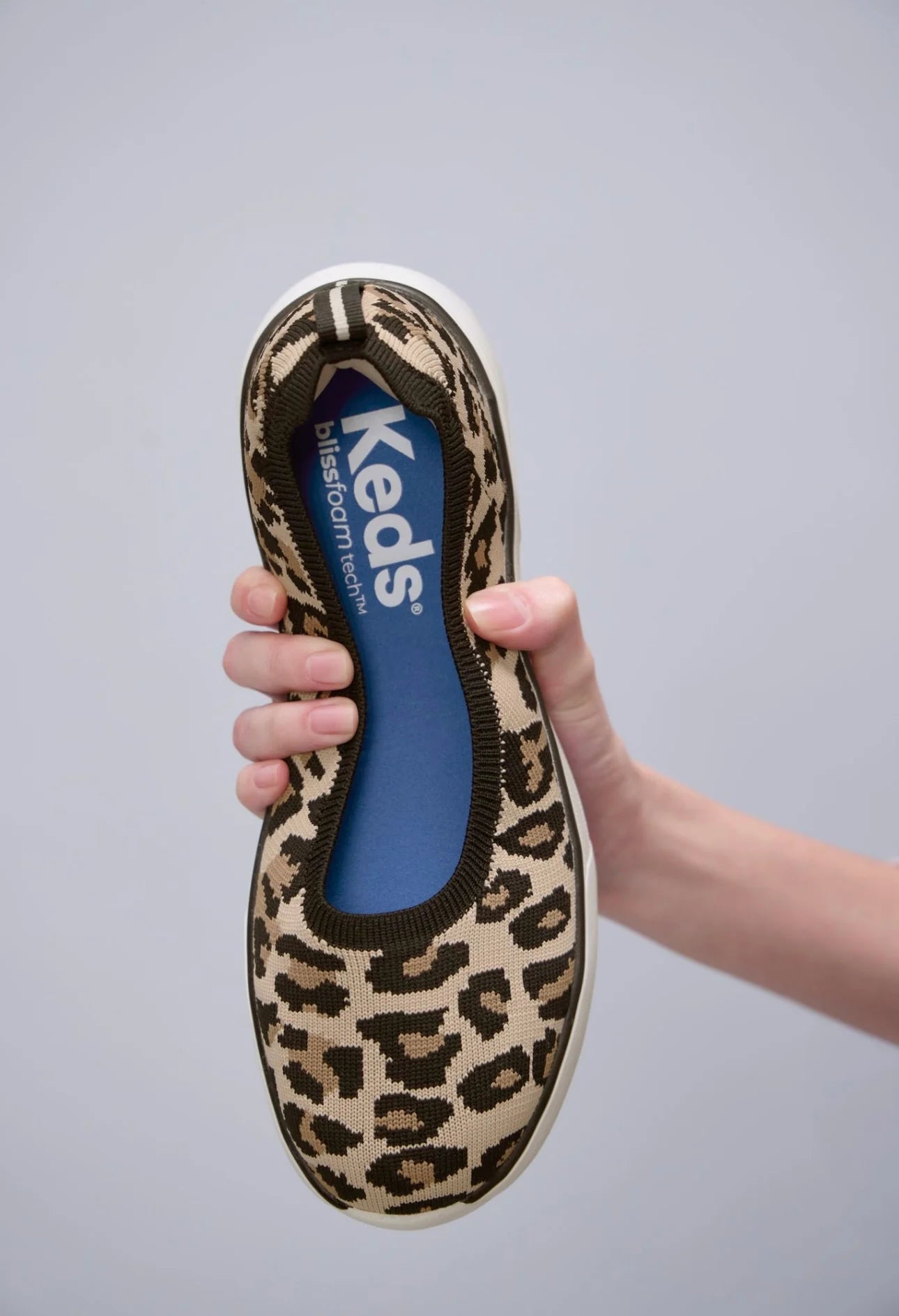 Keds BlissWalk Skimmer Knit Leo Tan Black slip on sneakers flexible leopard print knit upper shown in hand demonstrating lightweight comfort cushioned BlissFoam Tech insole removable washable design casual women’s footwear