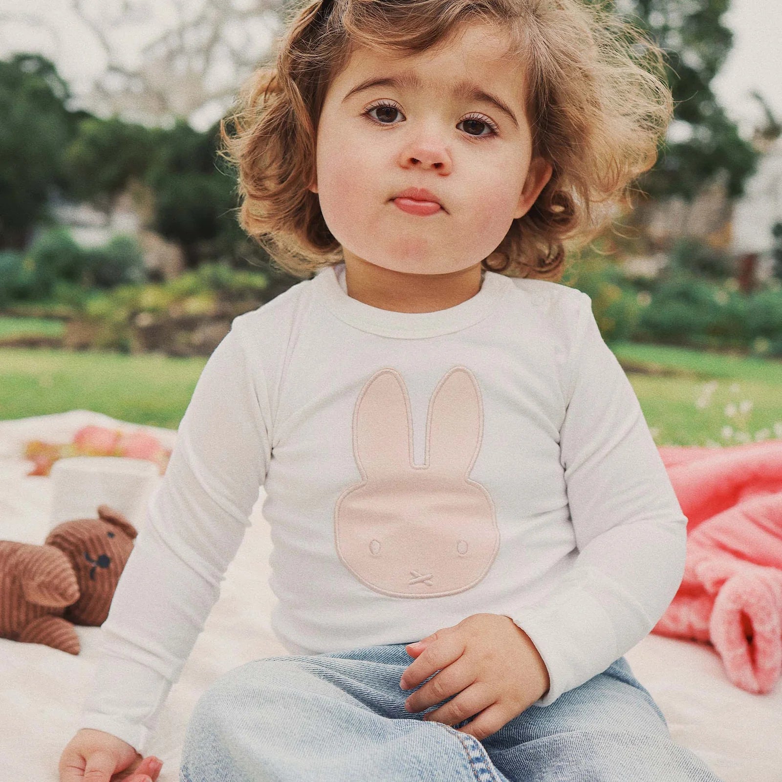 Toddler wearing the pink-applique Miffy bodysuit with blue jeans, close-up of chest detail outdoors.