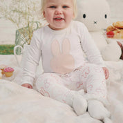 Baby sitting on a blanket in the Miffy bodysuit paired with pink printed leggings and snacks beside them.