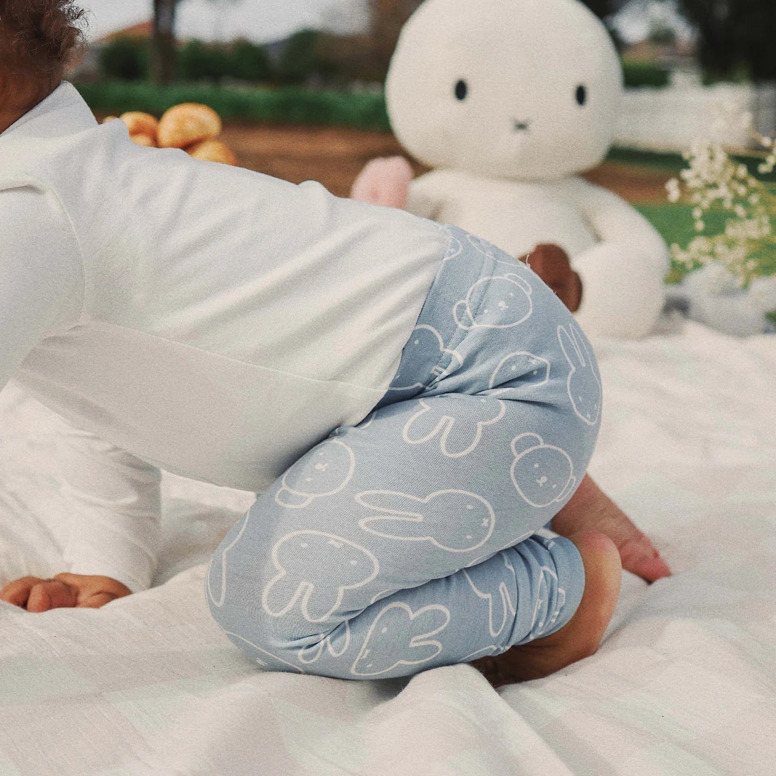 Close-up of Kynd Baby Miggy Leggings in moody blue with white Miffy bunny print, toddler sitting outdoors.