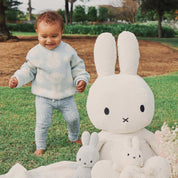 Toddler wearing Kynd Baby Miggy Leggings in moody blue with Miffy bunny print, standing on grass beside large Miffy plush.