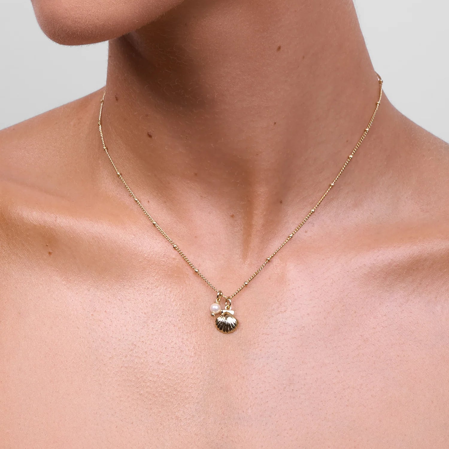 Model wearing LIBERTE Coast Silver Necklace, delicate scallop shell pendant and pearl charm on gold chain