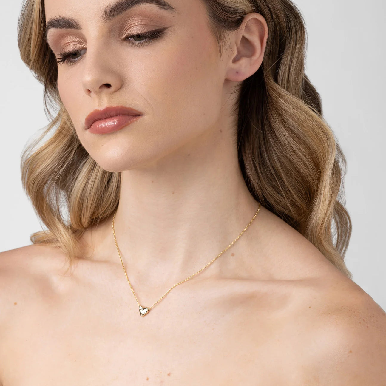 Woman wearing the LIBERTE Mariel Soft Gold Heart Necklace with a small, rounded gold heart pendant resting elegantly on her collarbone.