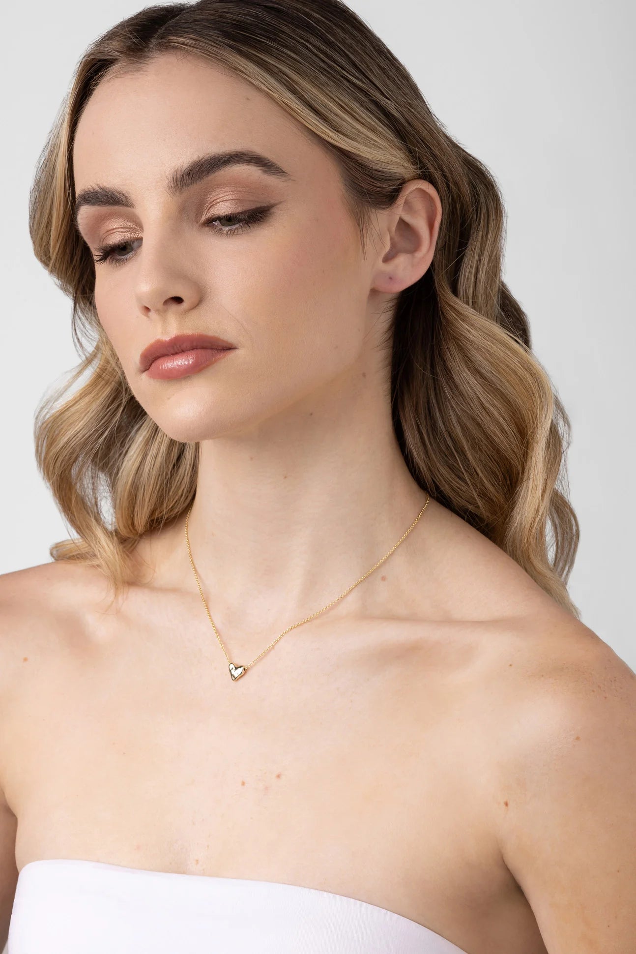 Woman wearing the LIBERTE Mariel Soft Gold Heart Necklace with a small, rounded gold heart pendant resting elegantly on her collarbone.