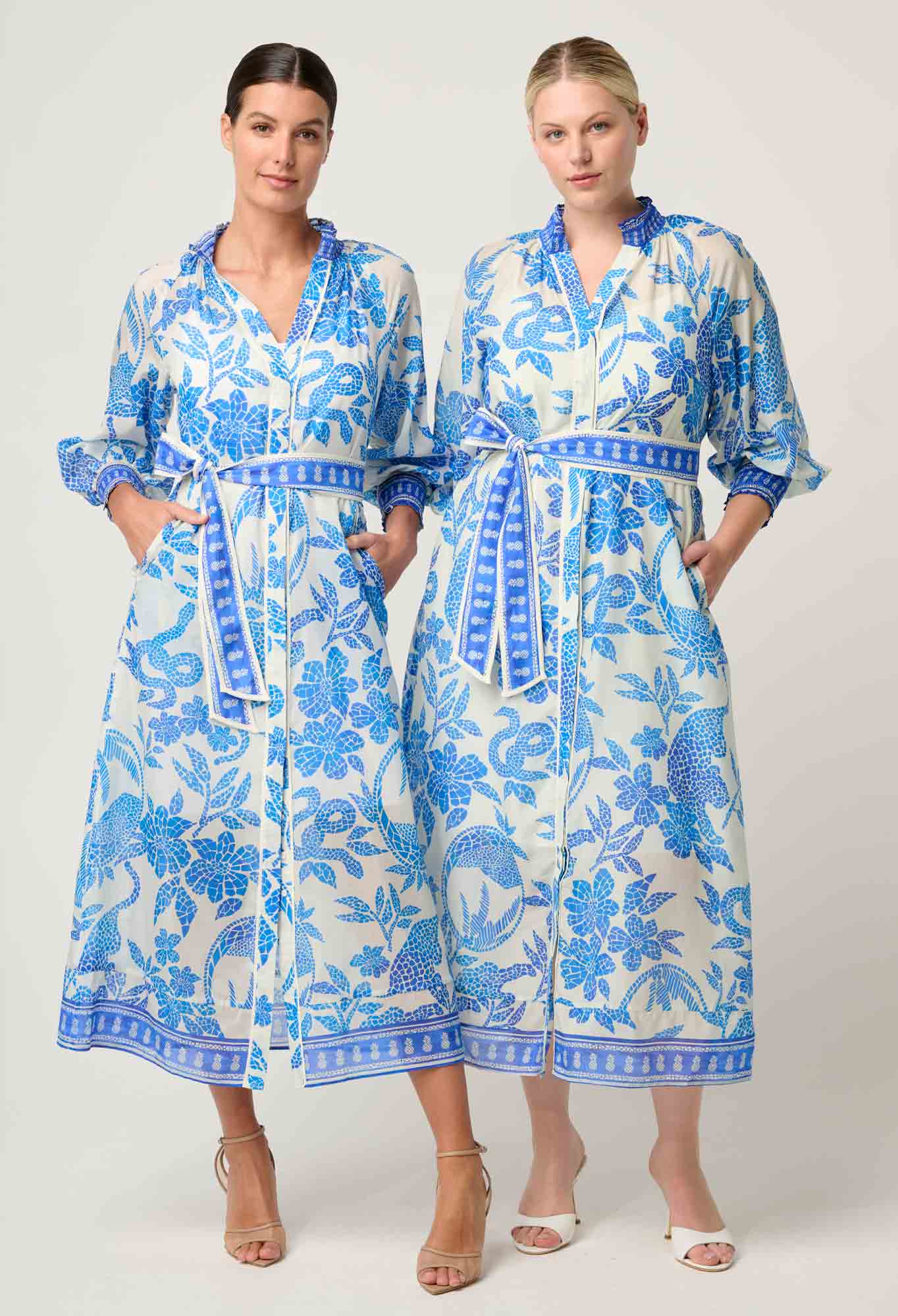 Two models wearing ONCE WAS Carmen Silk Cotton Maxi Dress in Azure Mosaic, styled with tie belts and blue floral pattern.