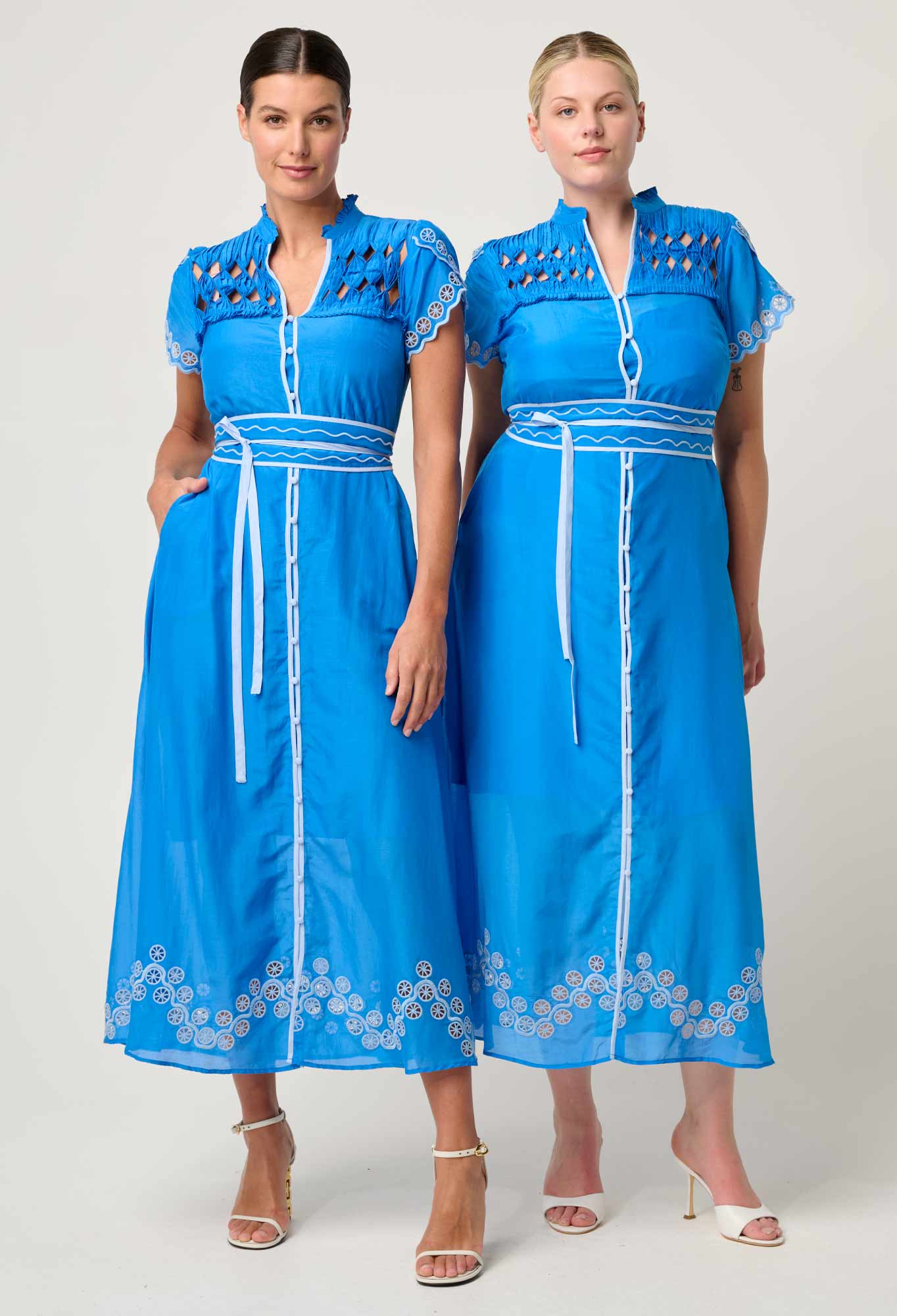 Two models wearing ONCE WAS Xanthia Diamond Smock Yoke Silk Cotton Embroidered Dress in Blue Topaz, styled with white embroidery and belted waist.