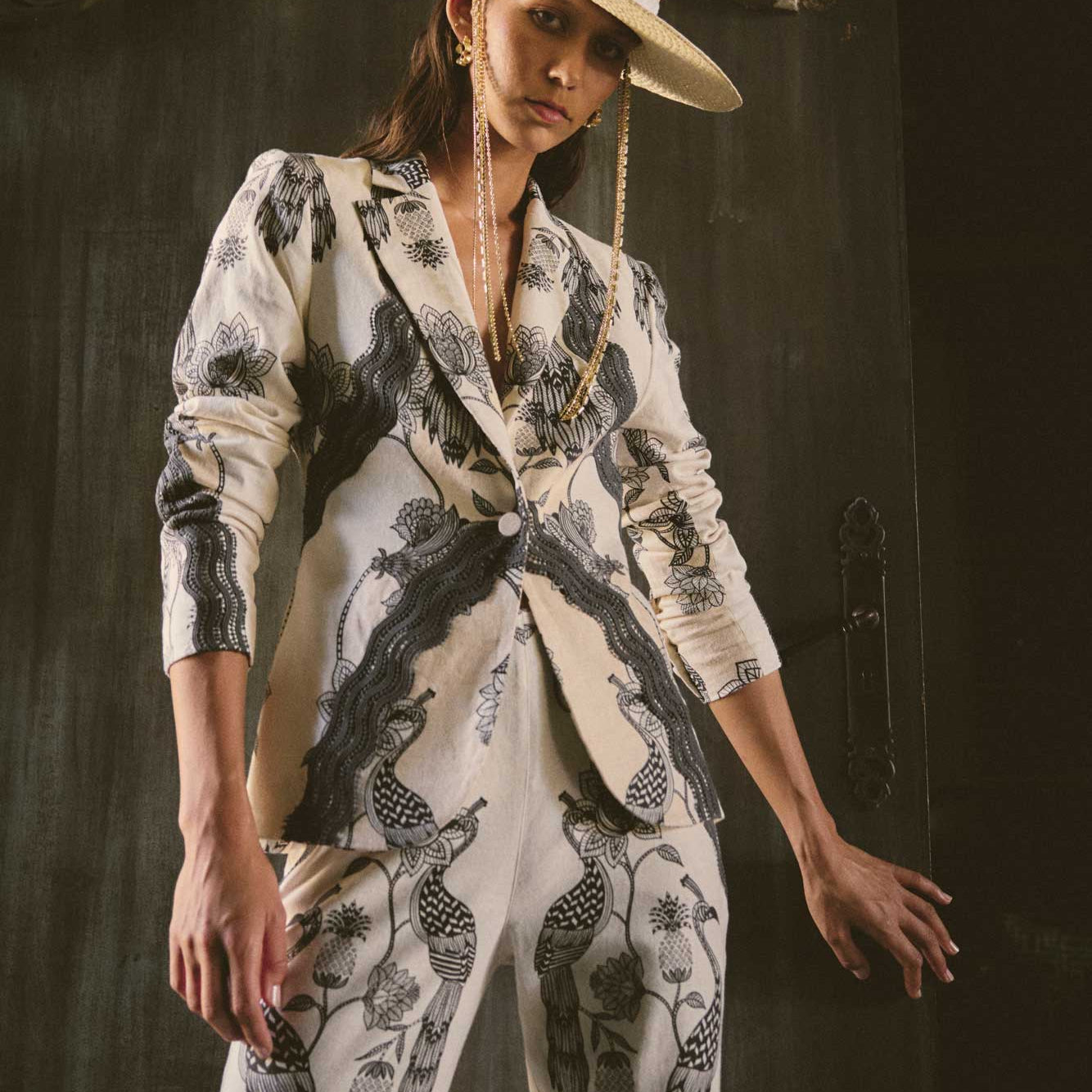 Woman wearing cream blazer and matching trousers with black bird and floral print styled with wide brim hat
