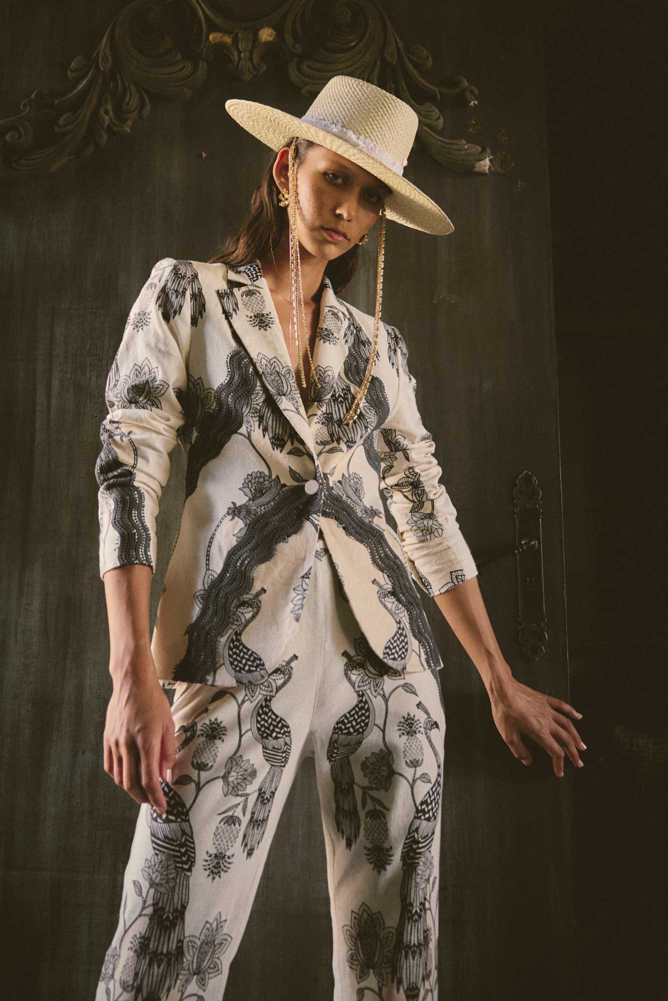 Woman wearing cream blazer and matching trousers with black bird and floral print styled with wide brim hat