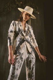 Woman wearing cream blazer and matching trousers with black bird and floral print styled with wide brim hat