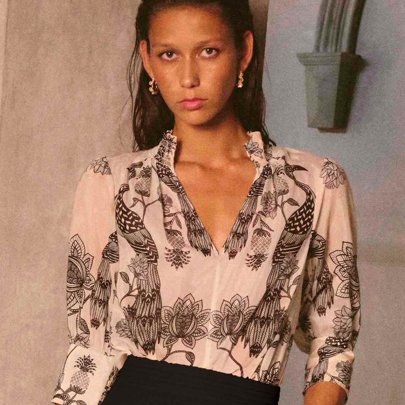Woman wearing cream blouse with black bird and floral print styled with black trousers editorial shot