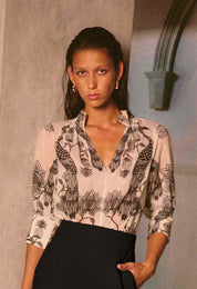 Woman wearing cream blouse with black bird and floral print styled with black trousers editorial shot