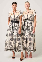 Two women wearing matching cream and black bird and floral print maxi dresses with belted waists