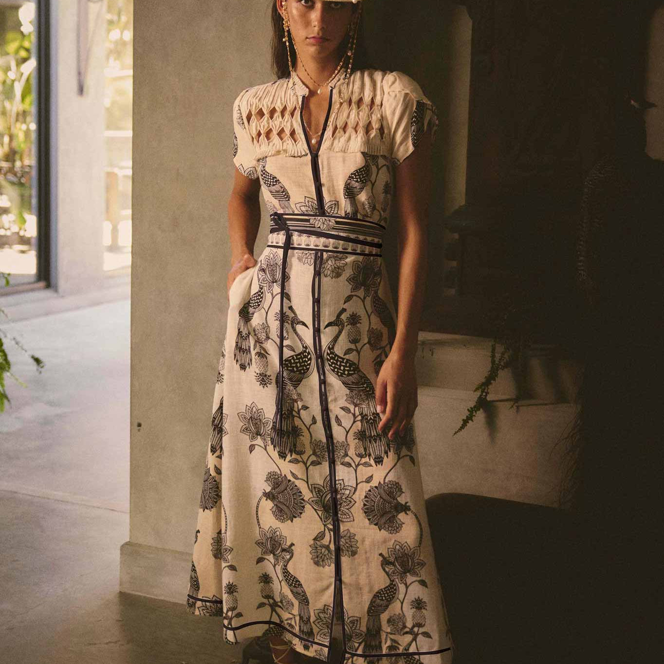 Woman wearing cream and black maxi dress with bird and floral print styled with a hat and sandals