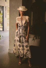 Woman wearing cream and black maxi dress with bird and floral print styled with a hat and sandals